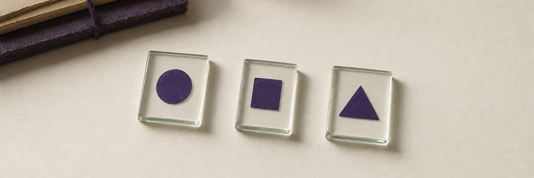 Three small rectangles of clear glass laid in a row on paper, each carrying a violet mark of a different shape and casting its own crisp shadow.